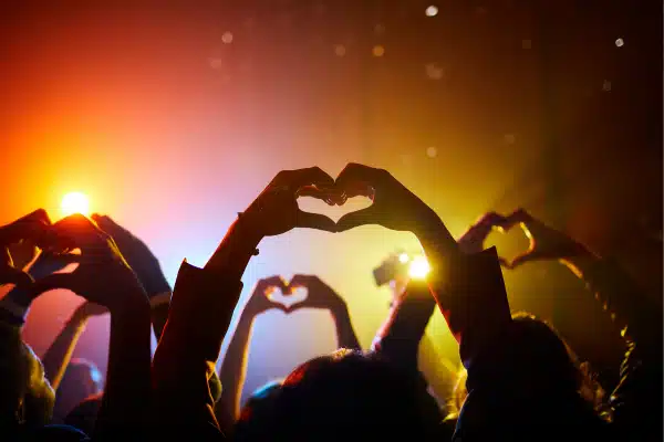 People at a concert making heart shapes with their hands, much like the iconic Taylor Swift gesture